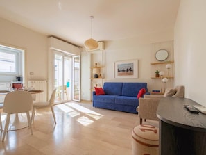 A modern living room with a blue sofa, a dining table with chairs, a round coffee table, and a kitchen area visible through an open door. - Versilia escape | 80 meters to the beach (Camaiore)