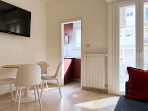 A modern living room with a flat-screen TV, a dining area with a table and chairs, a red accent wall, and a sliding glass door leading to a balcony. - Versilia escape | 80 meters to the beach (Camaiore)