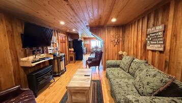 A cozy wooden interior with a sofa, a coffee table, a TV, and a kitchen area.