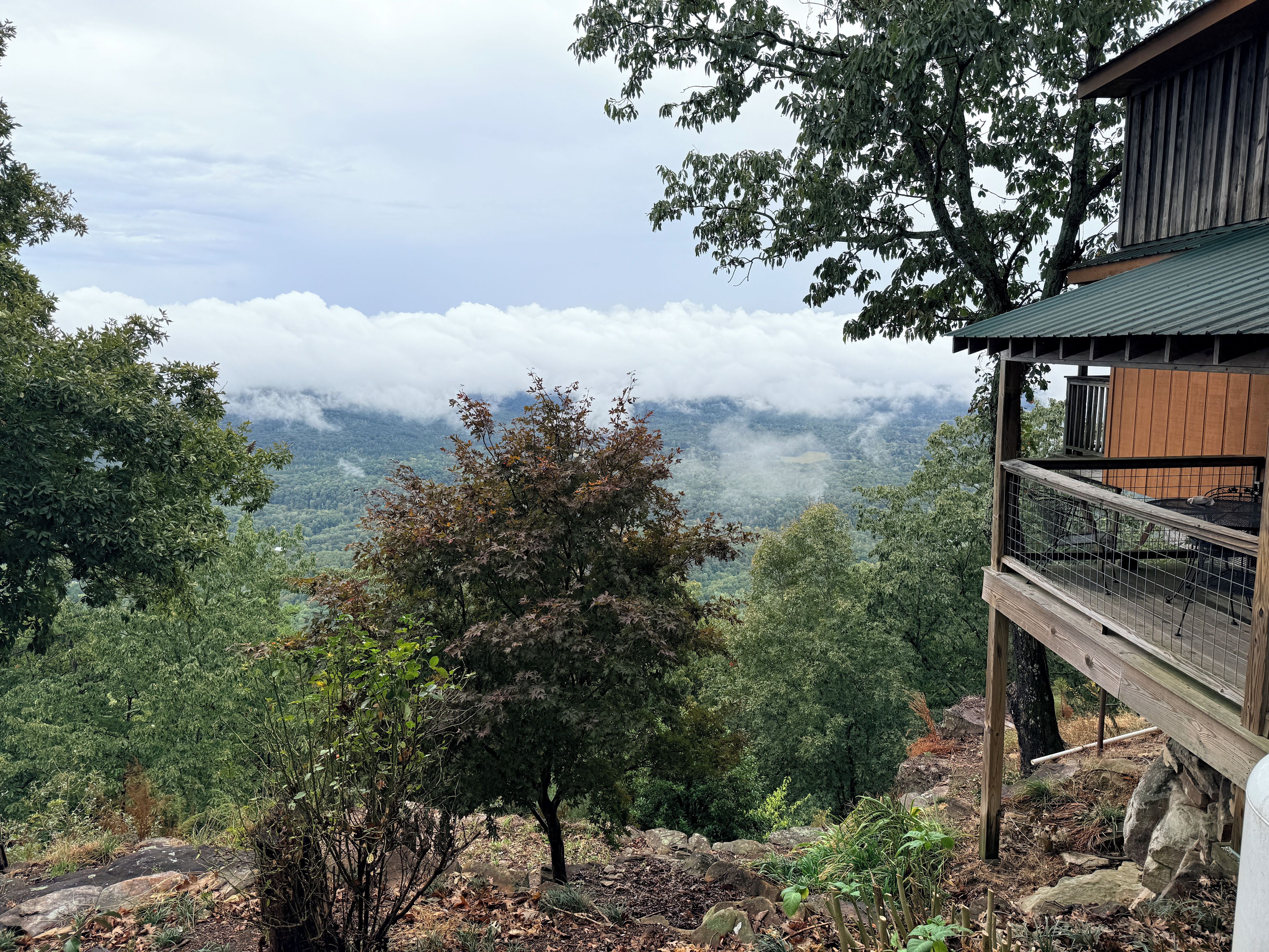 Eine Holzhütte mit einem Balkon mit Blick auf ein bewaldetes Tal und Wolken.