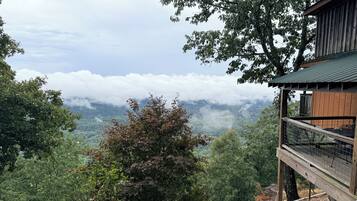 Eine Holzhütte mit einem Balkon mit Blick auf ein bewaldetes Tal und Wolken.
