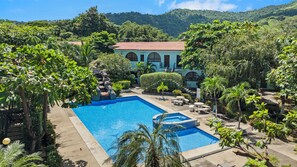 A swimming pool surrounded by lush greenery and a building with a red-tiled roof. - Newly renovated one-bedroom, one-bath ground unit at Turquoise Condominiums (Playas Del Coco)