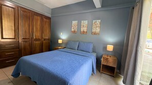 A bedroom with a large bed, wooden wardrobe, two bedside tables with lamps, and three wall-mounted paintings. - Newly renovated one-bedroom, one-bath ground unit at Turquoise Condominiums (Playas Del Coco)