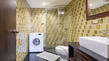 A compact bathroom with a washing machine, toilet, and shower area.