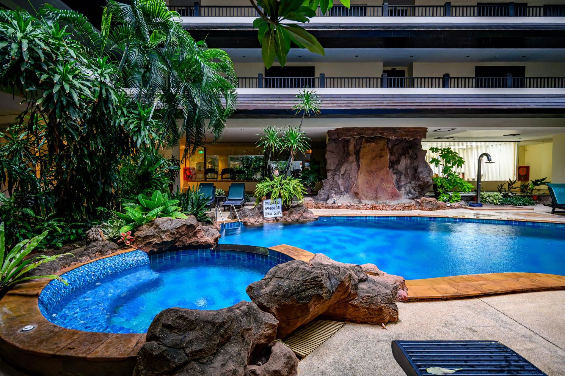 A hotel pool area with a hot tub, lounge chairs, and tropical plants.
