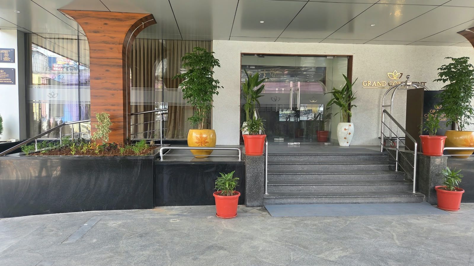 A hotel entrance with a modern design, featuring a staircase leading to the lobby, potted plants, and a sign indicating the hotel name.