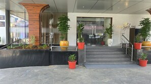 A hotel entrance with a modern design, featuring a staircase leading to the lobby, potted plants, and a sign indicating the hotel name.