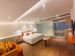 A modern hotel room with a bed, a seating area, a small table, and a television.