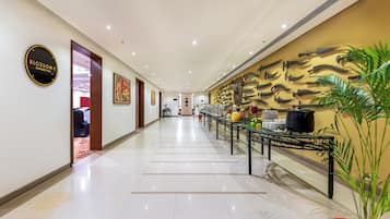 Pasillo de hotel con área de bufé, un letrero para el salón de banquetes y una pared con cubiertos colgantes.