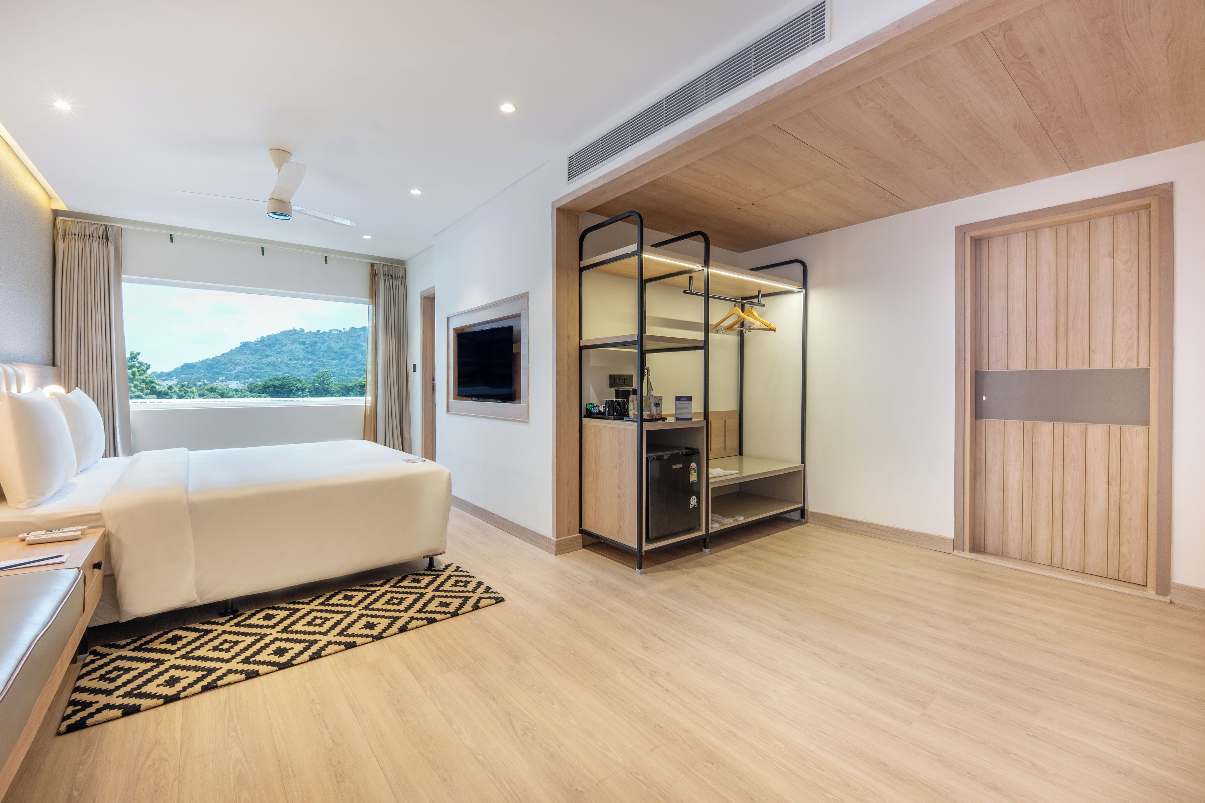 Habitación de hotel moderna con cama, televisor, minibar y vistas al exterior.