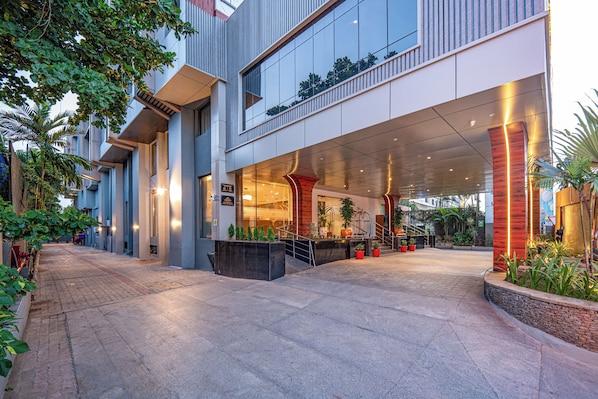 Un edificio moderno con entrada techada, área de estar al aire libre y plantas en macetas.
