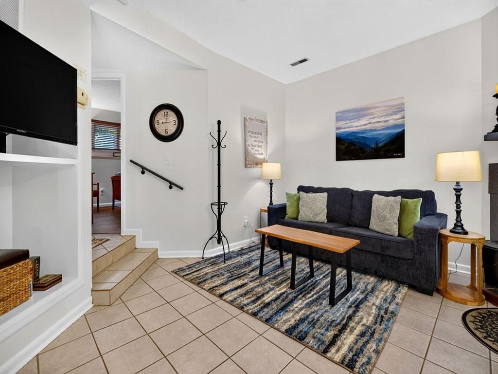 A living room with a sofa, a coffee table, a TV, a clock, and a painting on the wall.