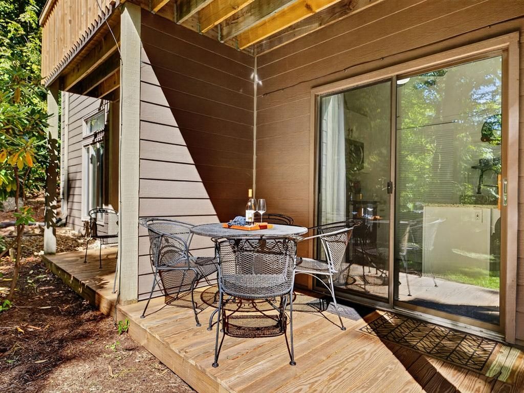 Une terrasse avec une table et des chaises, une plateforme en bois et une porte-fenêtre coulissante donnant sur un jardin.