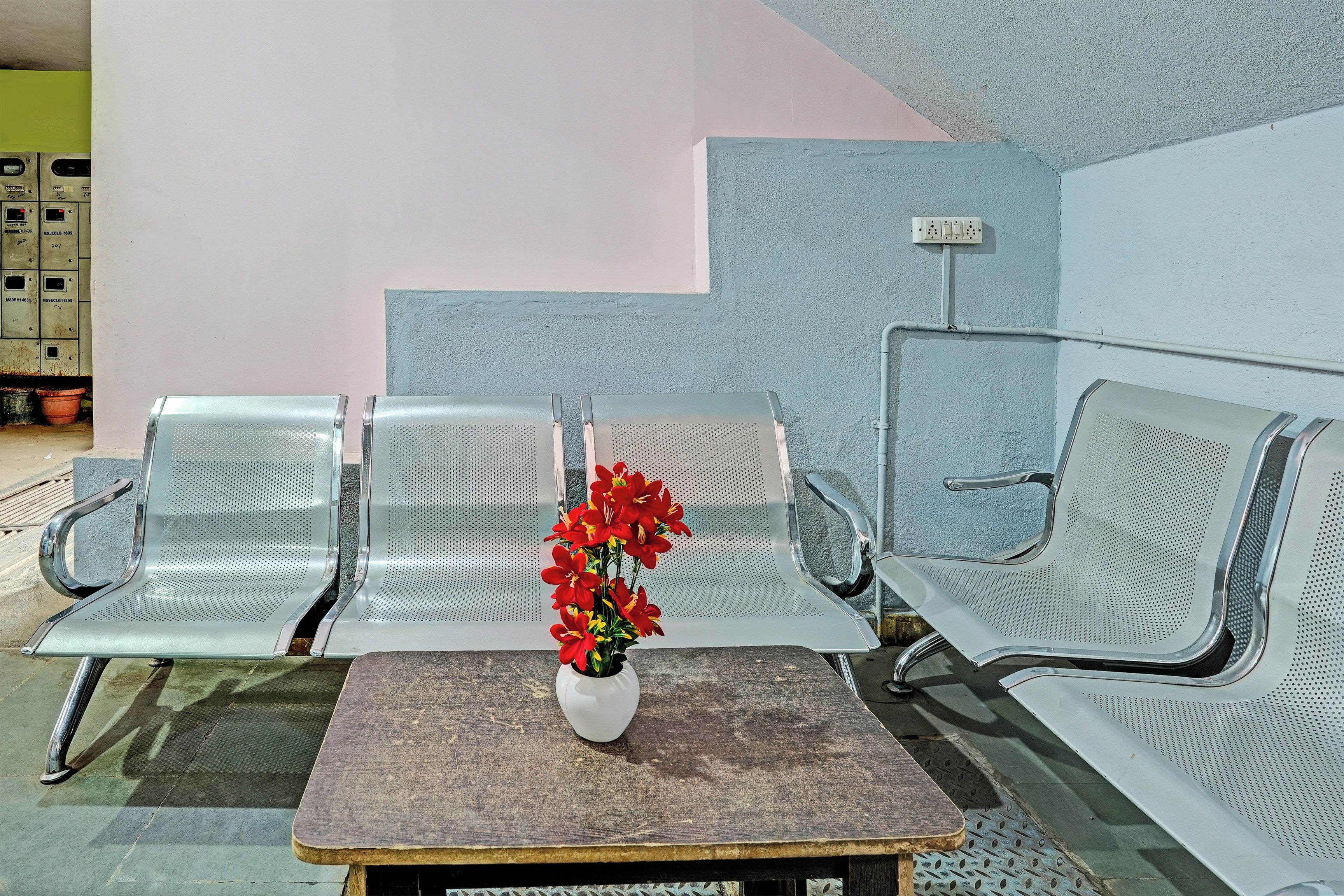 A waiting area with metal chairs, a small table with a vase of flowers, and a wall-mounted electrical outlet.
