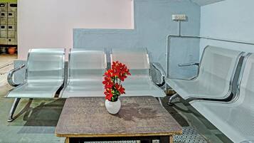 A waiting area with metal chairs, a small table with a vase of flowers, and a wall-mounted electrical outlet.