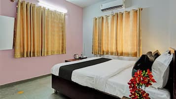 A hotel room with a bed, a nightstand, an air conditioner, and curtains.