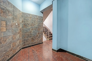 Un pasillo con pared de mármol y escalera con barandilla metálica.