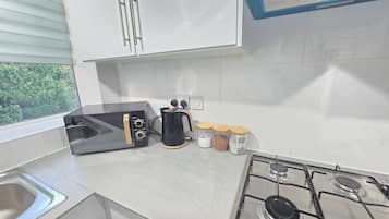 A kitchen with a gas stove, a coffee maker, and jars of spices.