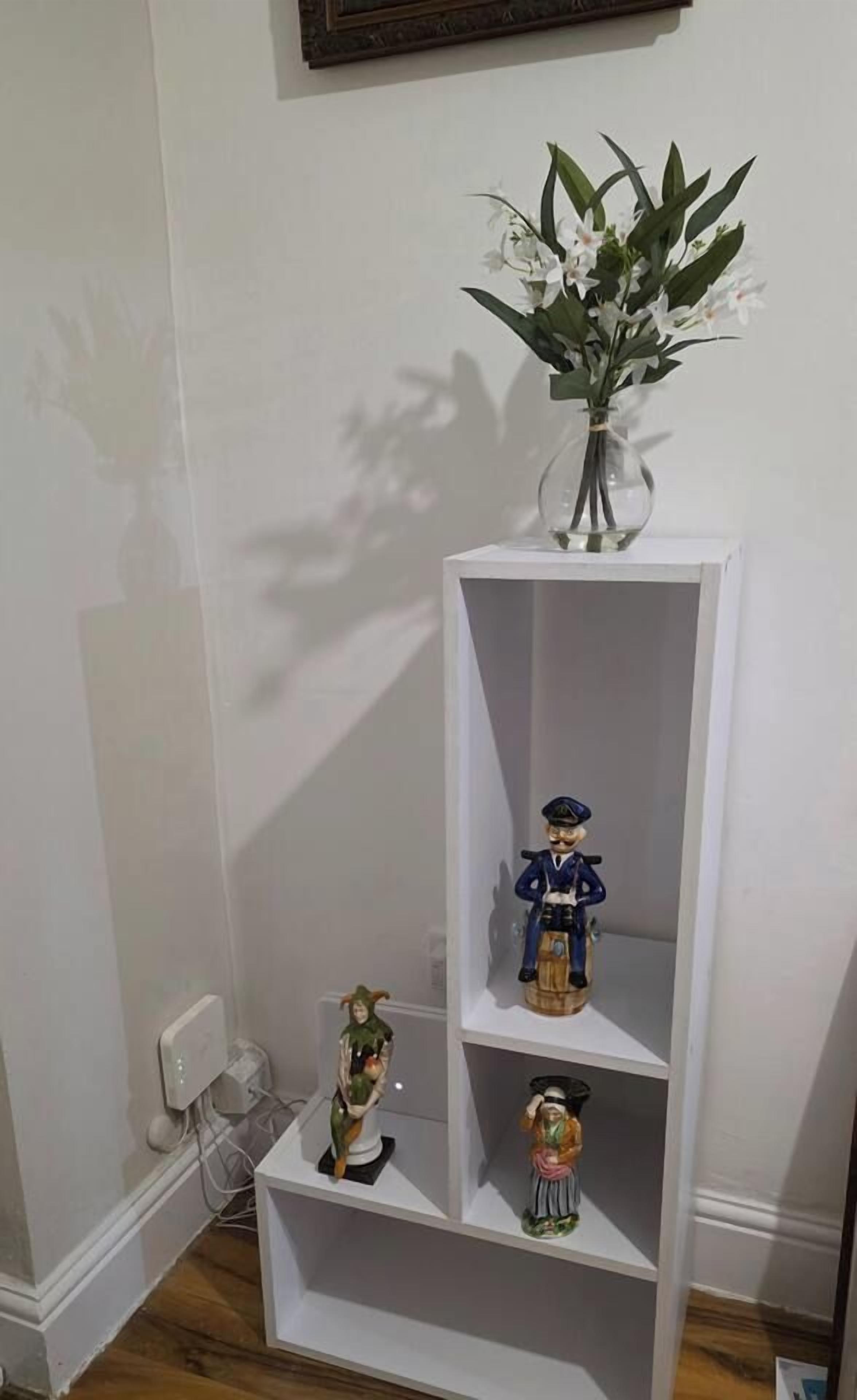 A white shelf with three figurines and a vase of flowers.
