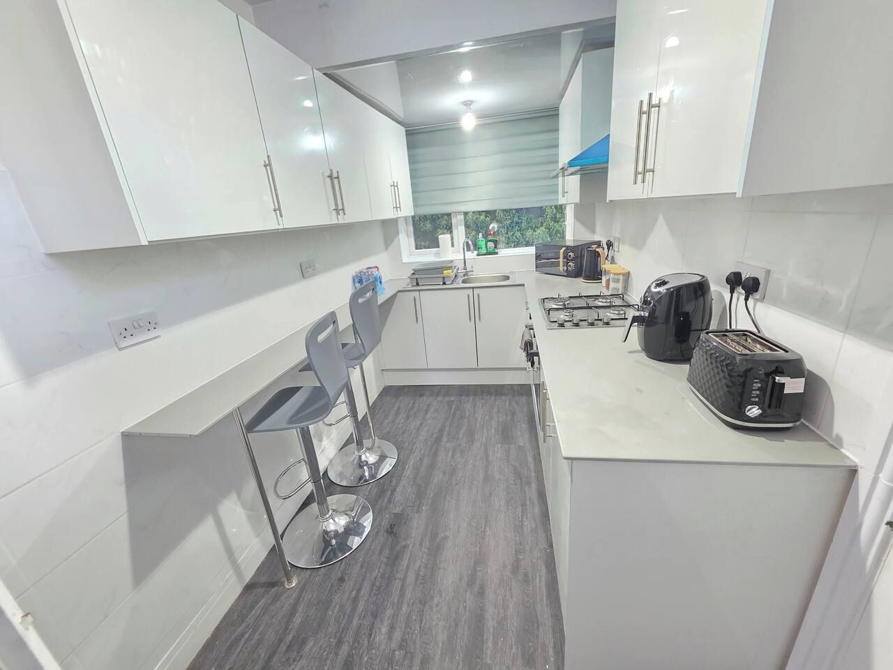 Une cuisine moderne avec des meubles blancs, un plan de travail gris et un tabouret de bar.
