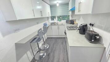A modern kitchen with white cabinets, a grey countertop, and a bar stool.