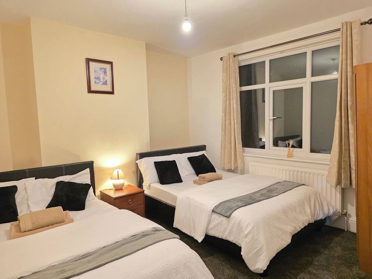 Une chambre d’hôtel avec deux lits, une fenêtre avec des rideaux, une lampe de chevet et un tableau encadré au mur.