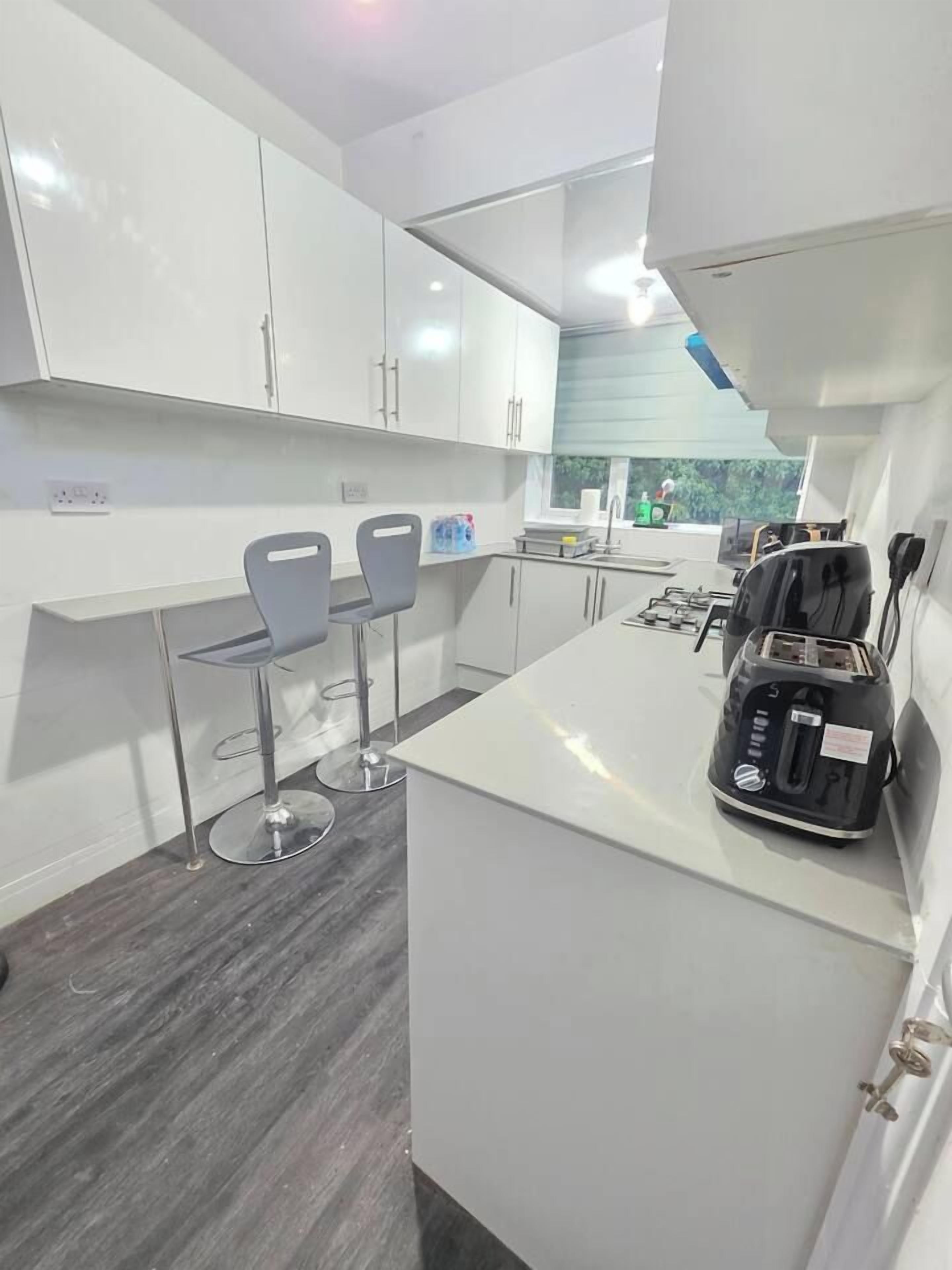 A modern kitchen with white cabinets, a countertop, two bar stools, and a toaster.