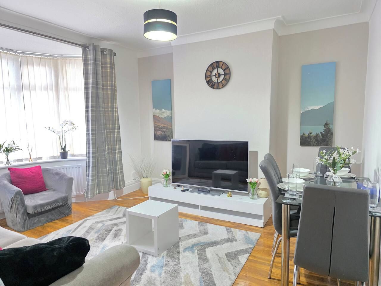 Una sala moderna con televisor de pantalla plana, un comedor con mesa de vidrio y un sofá con cojín rosa.