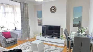 Una sala moderna con televisor de pantalla plana, un comedor con mesa de vidrio y un sofá con cojín rosa.