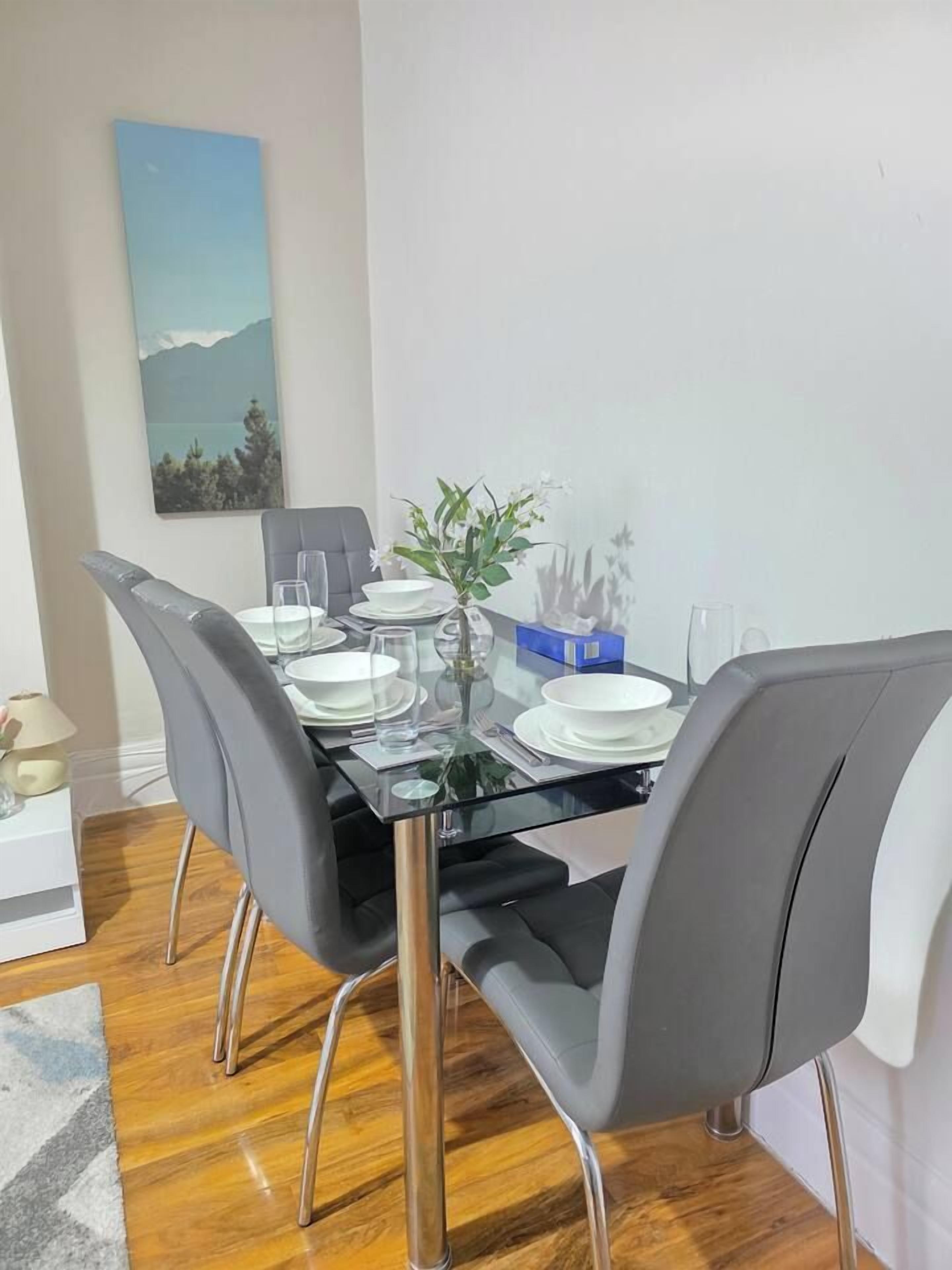 Un coin repas avec une table en verre, des chaises à revêtement gris et un tableau accroché au mur.
