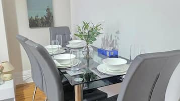 A dining area with a glass table, grey upholstered chairs, and a painting on the wall.