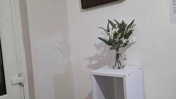 Une pièce avec une porte blanche, une étagère blanche ornée d’un vase de fleurs, un tableau encadré et une petite statue.