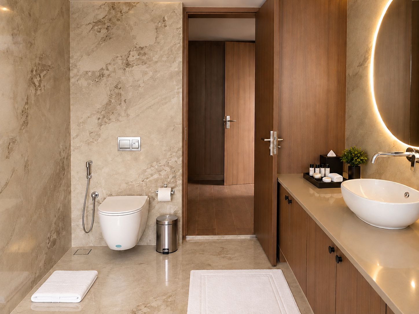 Un baño moderno con pared de mármol, inodoro, bidé, lavamanos con un espejo grande y una planta pequeña en el mueble.