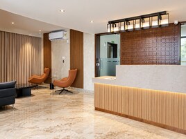 Un área de recepción moderna con piso de mármol, dos sillones de cuero, un mostrador de recepción y un equipo de aire acondicionado.