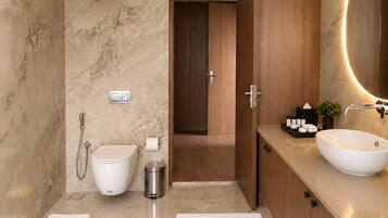 A modern bathroom with a marble wall, a toilet, a bidet, a sink with a large mirror, and a small plant on the vanity.