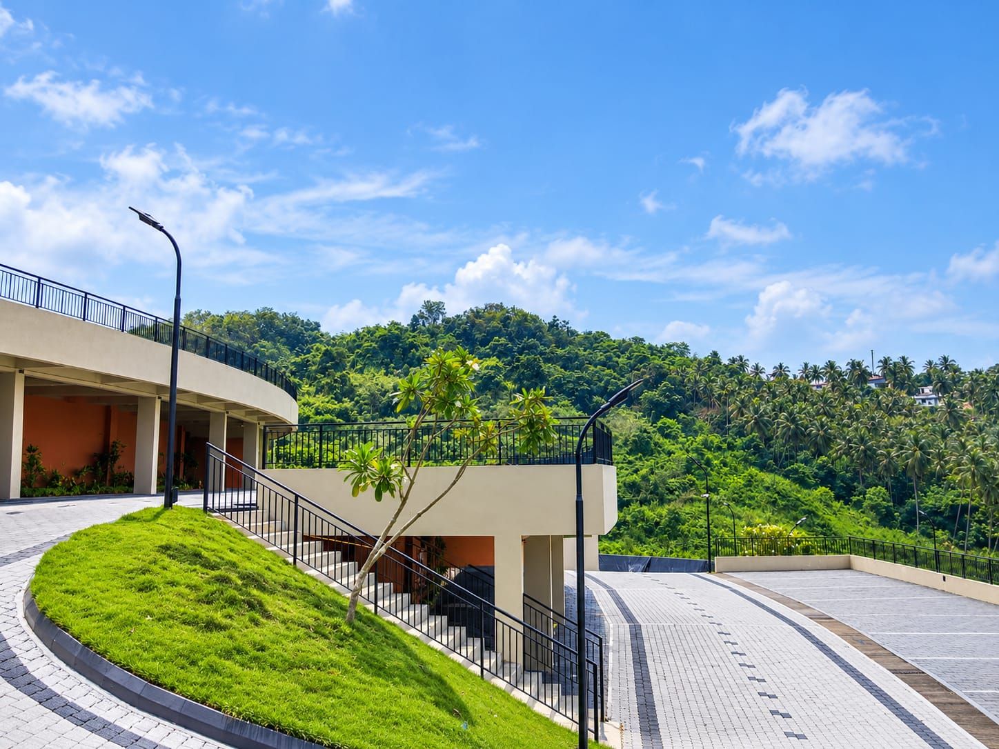 A modern building with a curved staircase, a flat roof, and a view of a lush green hill.