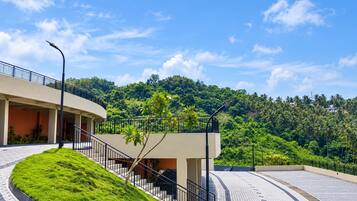 A modern building with a curved staircase, a flat roof, and a view of a lush green hill.