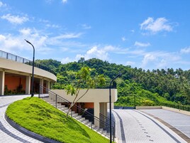 Un edificio moderno con una escalera curva, techo plano y vista a una colina verde exuberante.