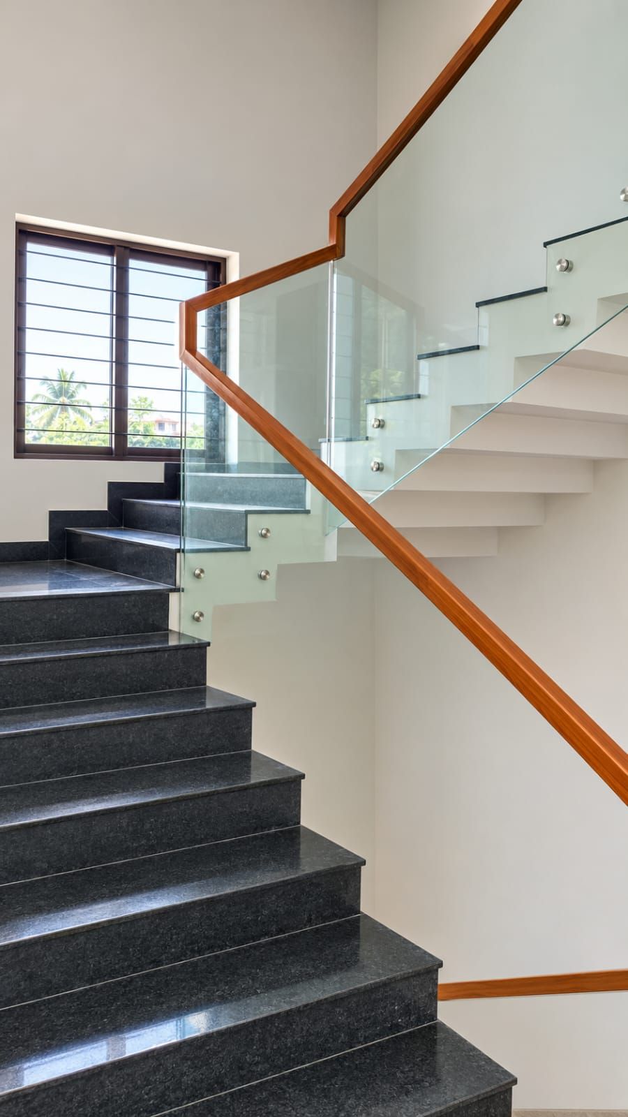 Eine moderne Treppe mit Glasgeländern und Holzhandläufen, die zu einer oberen Etage führt.