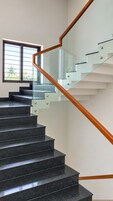 Una escalera moderna con barandillas de vidrio y pasamanos de madera, que lleva a un piso superior.