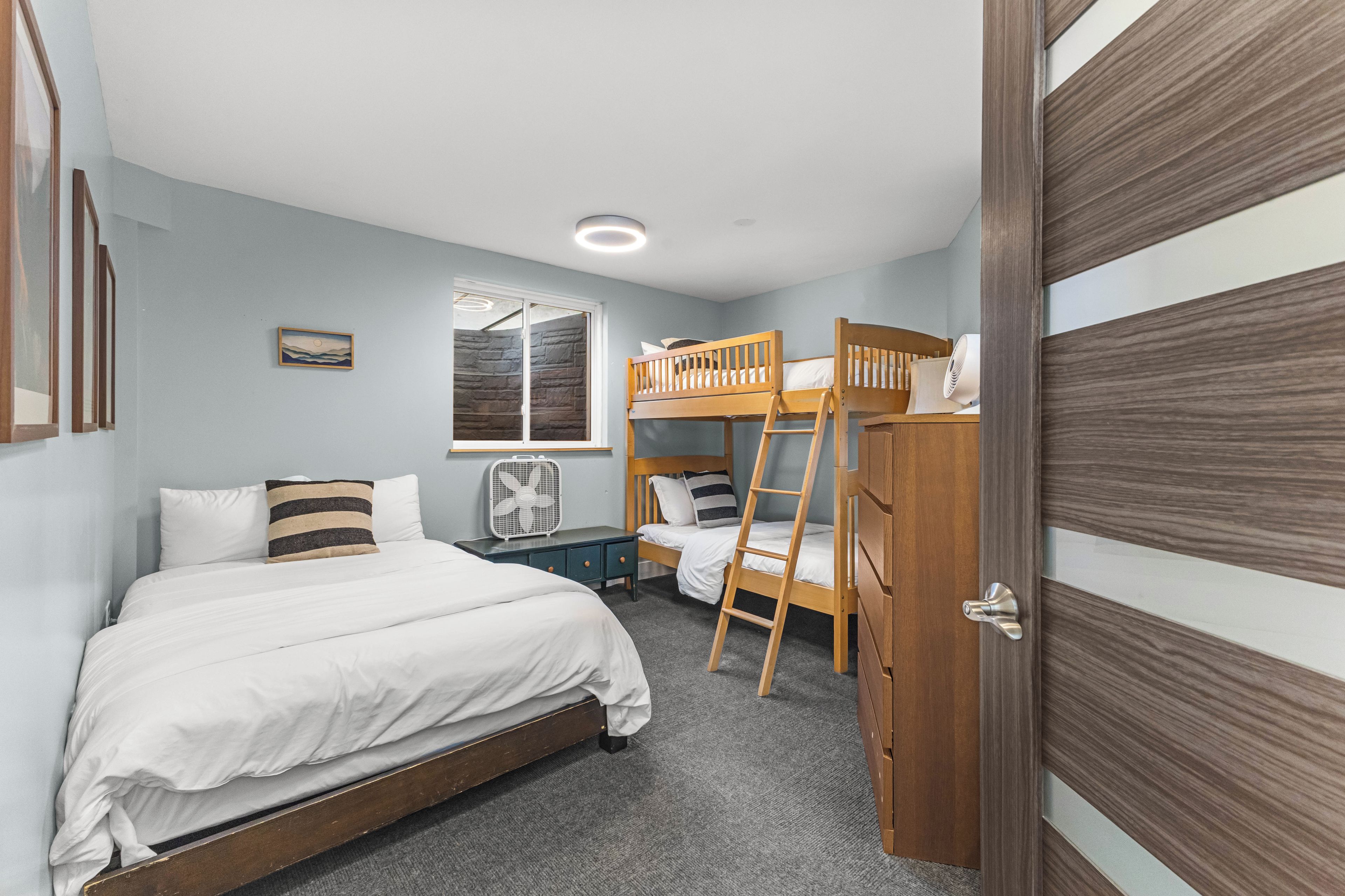 Un dormitorio con una cama litera, una cama individual, una ventana con vistas, un ventilador y una puerta.