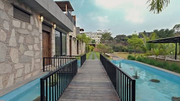Uma trilha que leva a uma piscina, com um muro de pedra de um lado e um prédio moderno com varandas.