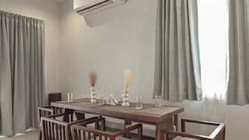 Uma sala de jantar com mesa e cadeiras de madeira, um ar condicionado e um ventilador de teto.