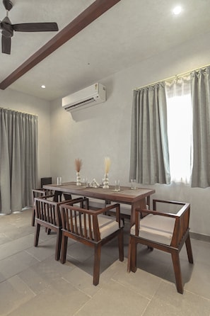 Uma sala de jantar com mesa e cadeiras de madeira, um ar condicionado e um ventilador de teto.
