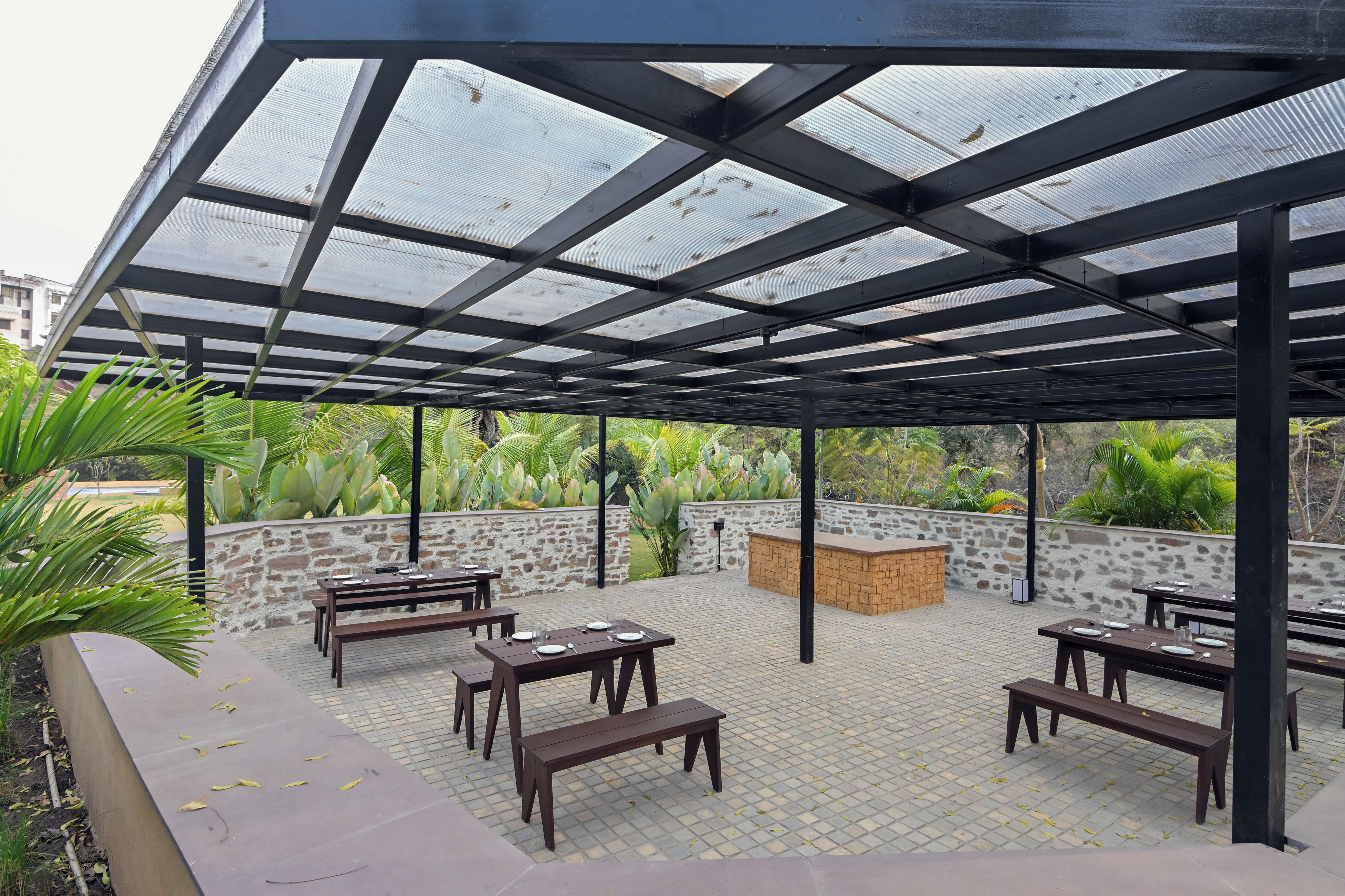 Un patio exterior con techo de vidrio, paredes de piedra y mobiliario de madera.