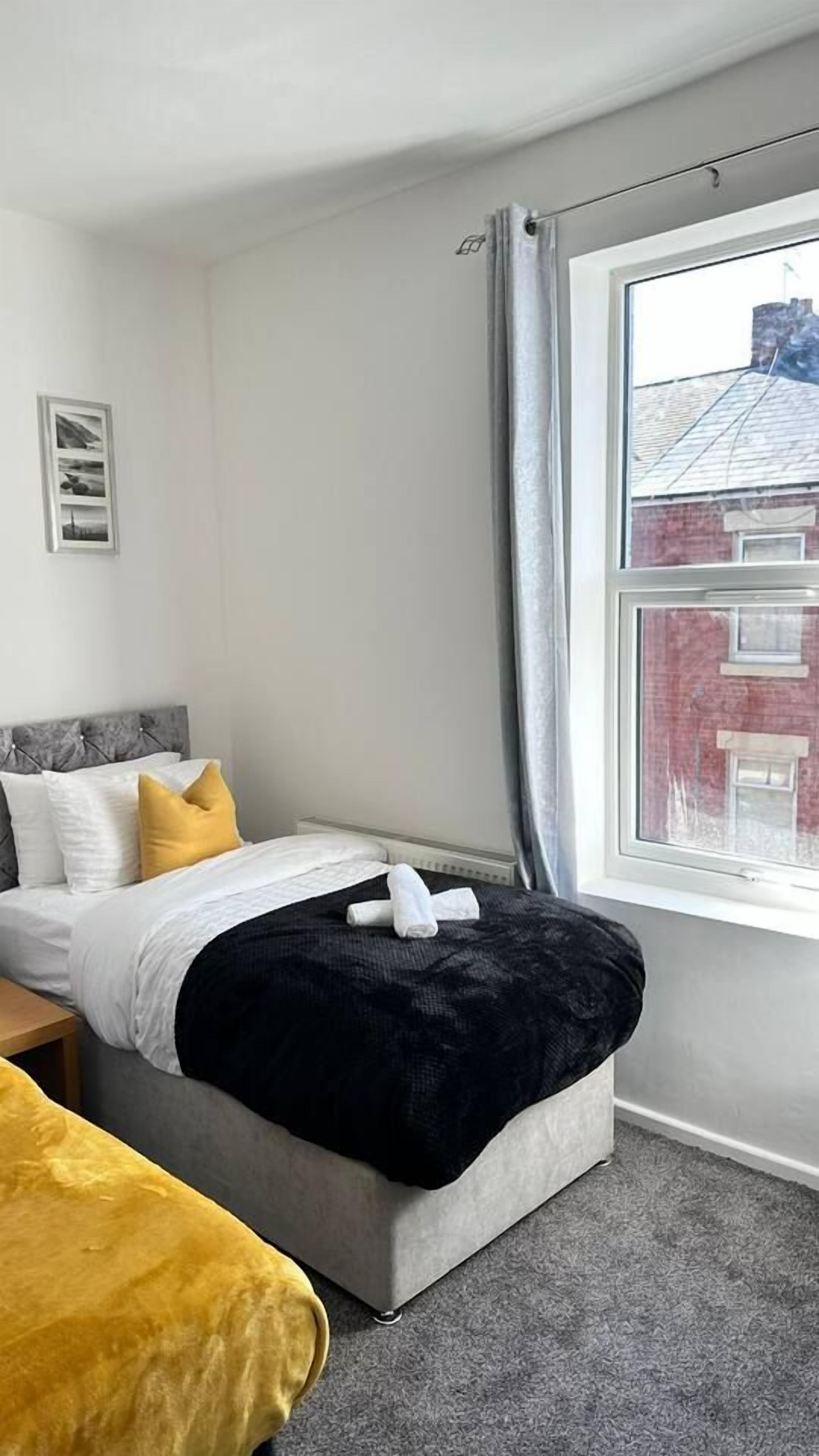 A bedroom with a bed, a bedside table, a window with curtains, and a view of a building outside.