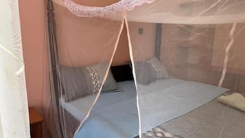 Una cama con mosquitero, almohadas y una colcha estampada.