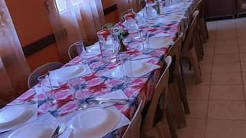 A dining area with a long table set for a meal, chairs around it, and kitchenware on the table.