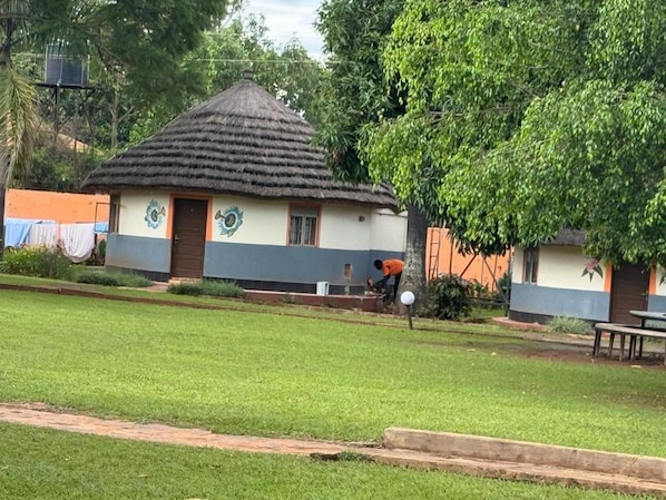 A building with a thatched roof, a door, and a window. There is a tree in front of the building.