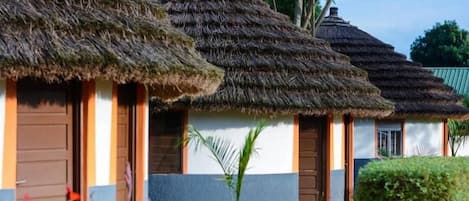 A row of thatched-roof huts with wooden doors and windows, surrounded by greenery.